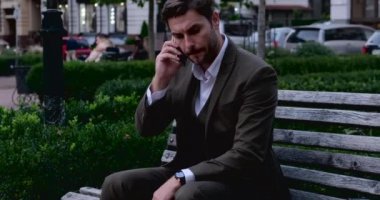 Park 'ta oturan genç işadamı ve telefonunda satış tabloları 
