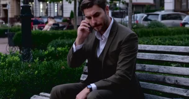 Junger Geschäftsmann sitzt im Park mit Verkaufscharts im Telefon — Stockvideo