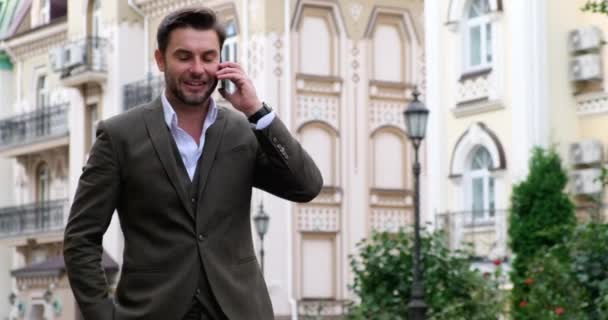 Pahalı takım elbiseli başarılı zarif erkek yönetici cep telefonuyla yürüyor. — Stok video