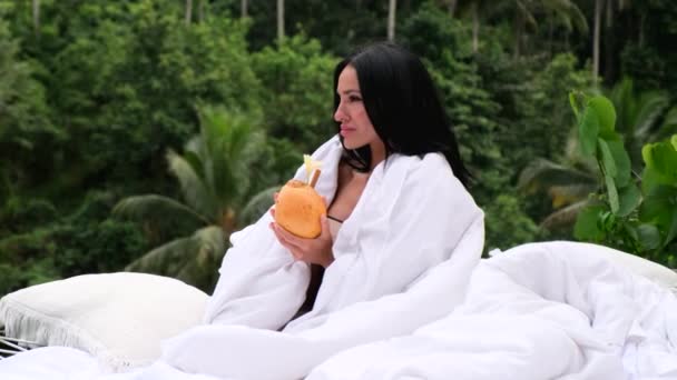 Девушка расслабляется и пьет кокосовый орех в бассейне на роскошной вилле на Бали — стоковое видео