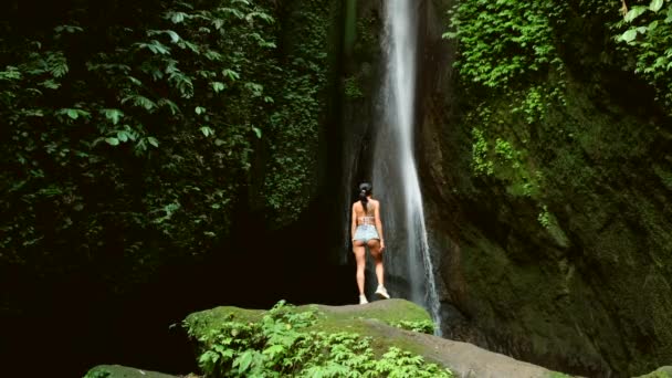 Sexy donna stand su roccia sulla bella cascata nella giungla accanto scogliera — Video Stock