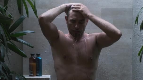 Mężczyzna pod prysznicem wśród tropikalnych kwiatów i liści. szampon i odżywka — Wideo stockowe