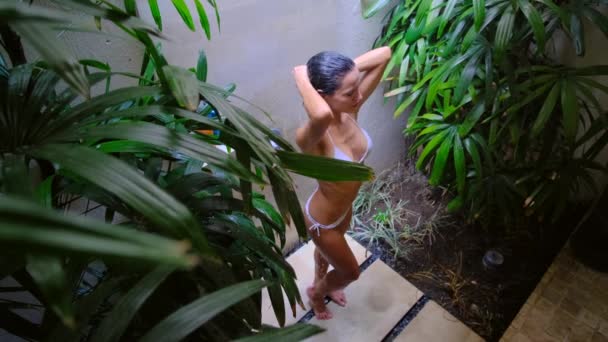 Chica en la ducha entre flores tropicales y hojas. champú y acondicionador — Vídeos de Stock