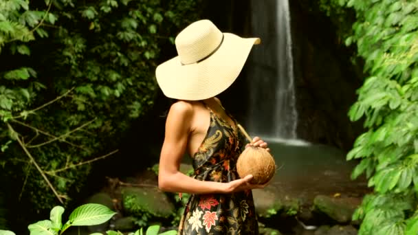 Жінка-туристка п'є кокосове молоко біля водоспаду у відпустці — стокове відео