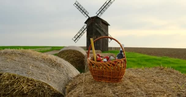 Деревянная старая мельница среди зеленой травы, плетеная корзина с продуктами, Пасха — стоковое видео