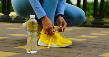Koşucuların ayakkabılarını yakın çekim. Kız sokakta spor ayakkabılarını giyer, şişe.