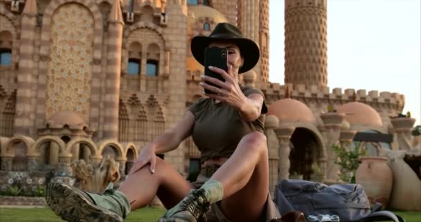 Menina bonita em estilo cowboy senta-se na grama, com o phone.mosque — Vídeo de Stock