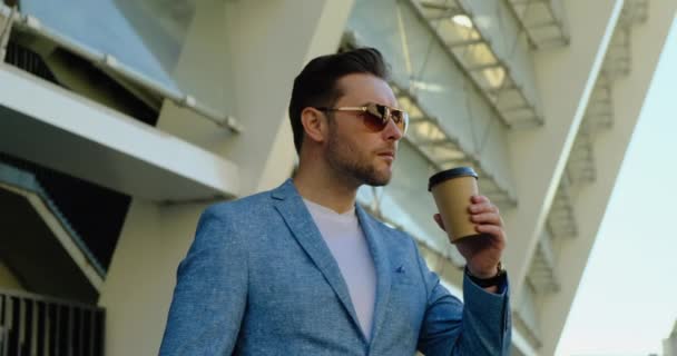 携帯電話でメガネテキスト付きジャケットにコーヒーを持つアメリカ人男性｜ビットコイン — ストック動画