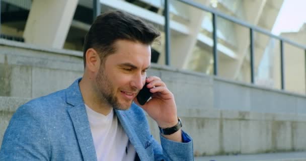 Bonito jovem usando telefone inteligente enquanto está de pé ao ar livre com café — Vídeo de Stock