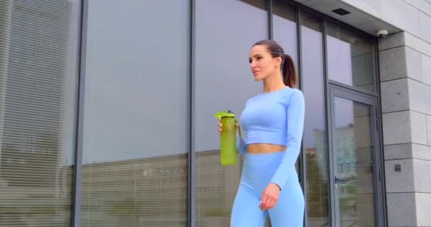 Спортсменка в модной одежде пьет воду после тренировки. Жажда, обезвоживание — стоковое видео