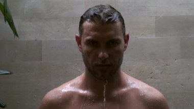 Çıplak gövdeli yakışıklı adam tropikal bir evde duş alıyor.