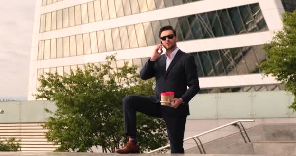 Kluger Geschäftsmann mit Brille, der in der Stadt telefoniert und Kaffee trinkt — Stockvideo