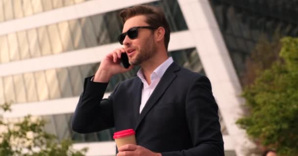 Uomo d'affari intelligente in bicchieri parlare al telefono in città e in possesso di caffè — Video Stock