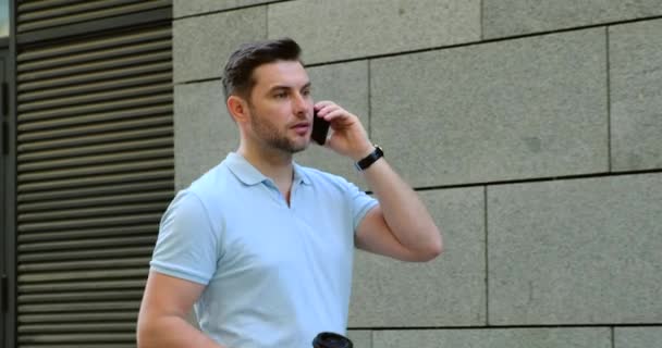 Primer plano sonriente hombre con café hablando de teléfono móvil cerca de la oficina. hermoso día — Vídeos de Stock