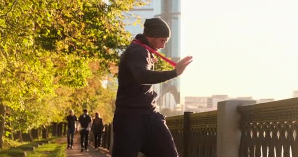 Спортсмен делает упражнения с фитнес-резиновой лентой City and Park autumn — стоковое видео