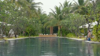Erkek turist, Maldivler 'de tropik bir tatil köyünde egzotik lüks bir havuzda yüzüyor. Manzara rahatlamayı, rahatlamayı ve cennet adasının özünü yansıtır. Doğayla, sağlıkla, sakin okyanus atmosferiyle seyahat eder.