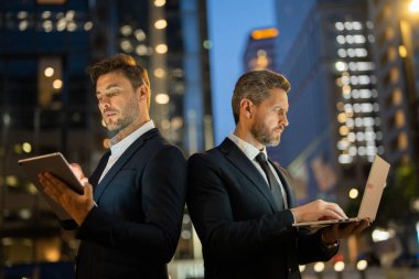 İki işadamı arka arkaya gece New York 'ta tablet ve dizüstü bilgisayardaki verileri analiz ediyor. Erkek profesyoneller rekabet ve kararlılığı yansıtır. Sahne teknolojiyi, iş odaklarını ve kentselliği vurguluyor