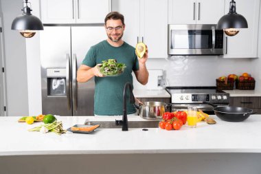 Şef parlak, modern bir mutfakta taze sebzeli avokado salatası yapıyor. Erkek aşçı vejetaryen gıda hazırlıklarına odaklanır. Atmosfer sağlıklı yaşam tarzını ve organik bileşenleri yansıtır..