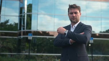 İşletme yöneticisi modern cam ofis binasının önünde kollarını kavuşturmuş poz veriyor. Takım elbiseli yetişkin adam liderlik, güven ve kurumsal başarıyı temsil ediyor. Sahne iş gücünü ve otoriteyi gösteriyor