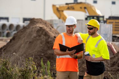 İki miğfer müfettişi bir şantiyede bina belgelerini inceliyor. Erkek mühendisler proje planlarını tartışıyor. Mimari, denetim ve endüstriyel kalkınma taşır.