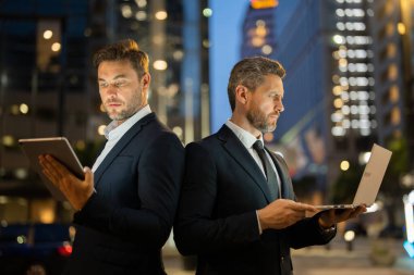 İki işadamı, geceleri New York sokaklarında tablet ve laptop kullanarak dijital bilgileri analiz ediyor. Erkek profesyoneller odaklanma ve kararlılık gösterirler. Sahne teknolojiyi, şehir enerji işini ön plana çıkarıyor.