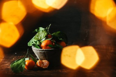 Gri beton plakalı yeşil yapraklı mandalinalar koyu bir arka planda tank etkisi yaratıyor.