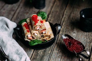  Tahta arka planda kırmızı havyar balığı ve krem peynirli krep.