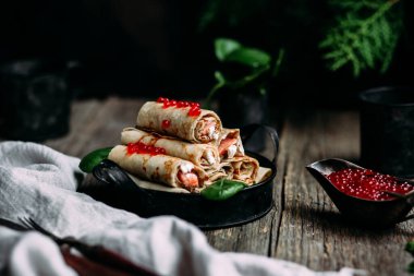  Tahta arka planda kırmızı havyar balığı ve krem peynirli krep.