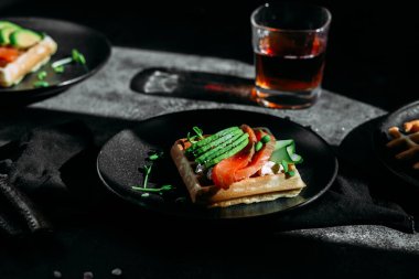 Beyaz tabakta somon, avokado ve krem peynirli Belçika waffleları. Masada sağlıklı bir kahvaltı.