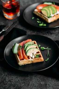 Beyaz tabakta somon, avokado ve krem peynirli Belçika waffleları. Masada sağlıklı bir kahvaltı.