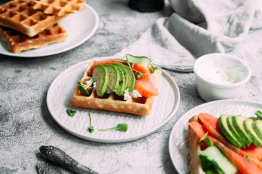 Beyaz tabakta somon, avokado ve krem peynirli Belçika waffleları. Masada sağlıklı bir kahvaltı.