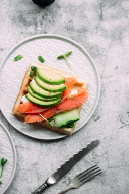 Beyaz tabakta somon, avokado ve krem peynirli Belçika waffleları. Masada sağlıklı bir kahvaltı.