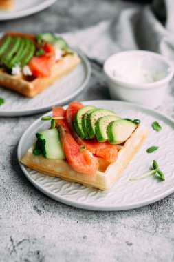 Beyaz tabakta somon, avokado ve krem peynirli Belçika waffleları. Masada sağlıklı bir kahvaltı.