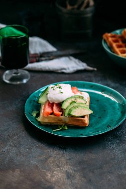 Somonlu Belçika waffleları, haşlanmış yumurta, avokado ve turkuaz tabakta krem peynir. Masada sağlıklı bir kahvaltı.