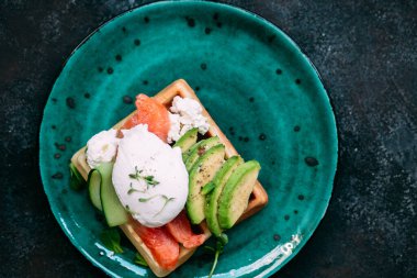 Somonlu Belçika waffleları, haşlanmış yumurta, avokado ve turkuaz tabakta krem peynir. Masada sağlıklı bir kahvaltı.