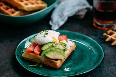 Somonlu Belçika waffleları, haşlanmış yumurta, avokado ve turkuaz tabakta krem peynir. Masada sağlıklı bir kahvaltı.