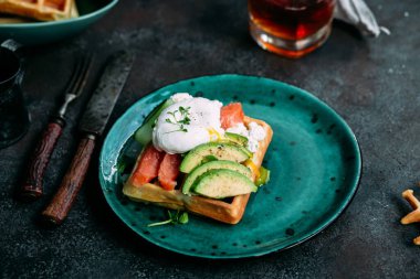 Somonlu Belçika waffleları, haşlanmış yumurta, avokado ve turkuaz tabakta krem peynir. Masada sağlıklı bir kahvaltı.