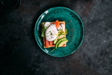Somonlu Belçika waffleları, haşlanmış yumurta, avokado ve turkuaz tabakta krem peynir. Masada sağlıklı bir kahvaltı.