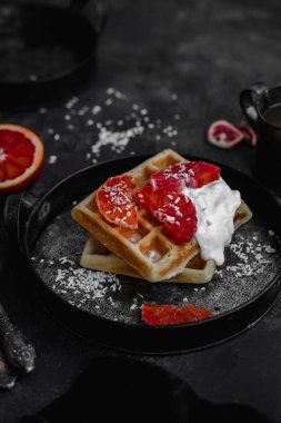Koyu bir tabakta kanlı portakallı Belçika waffle 'ları. Siyah fotoğraf