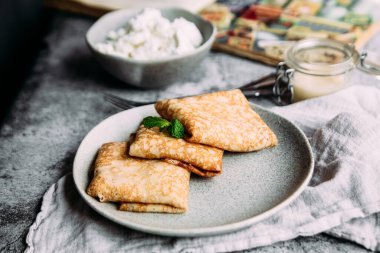 Ev yapımı süzme peynirli krep, yaban mersini ve gri tabakta limon ezmesi.
