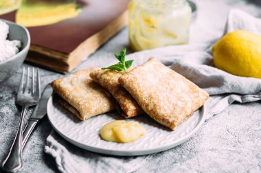 Ev yapımı süzme peynirli krep, yaban mersini ve gri tabakta limon ezmesi.