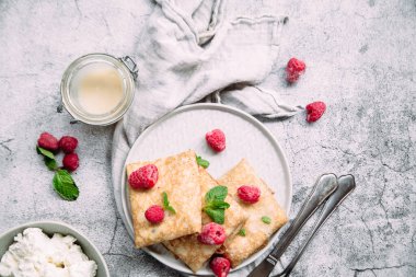 Ev yapımı süzme peynirli krep, ahududu, gri tabak.