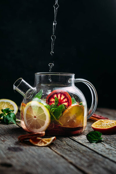  Чайный брызг с цитрусовыми и мятой в стеклянном чайнике на темном фоне. Брызги чая