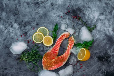Çiğ somon bifteği, otlu, buzlu ve limonlu gri arka plan.