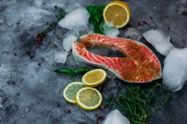 Çiğ somon bifteği, otlu, buzlu ve limonlu gri arka plan.