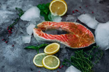 Çiğ somon bifteği, otlu, buzlu ve limonlu gri arka plan.