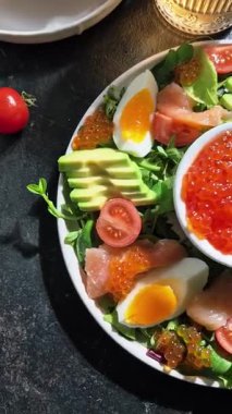 Salad with trout, caviar, avocado, eggs and red caviar in a white plate