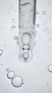 Şeffaf sıvı serum veya özü içinde hava kabarcıkları olan cam pipet damlatıcısının dikey makro videosu. Laboratuvar araştırması, hidrasyon ve cilt bilimi kavramı.