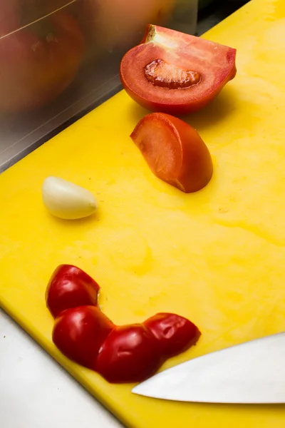 Pimentas de tomate fatiadas e alho em uma tábua amarela — Fotografia de Stock