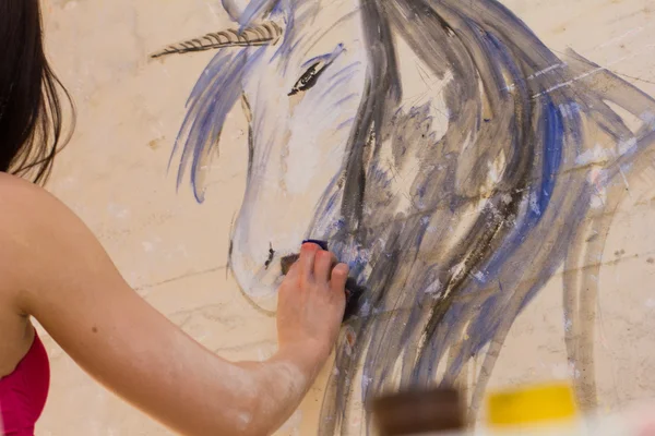 Beautiful girl artist paints on the wall of the unicorn — Stock Photo, Image